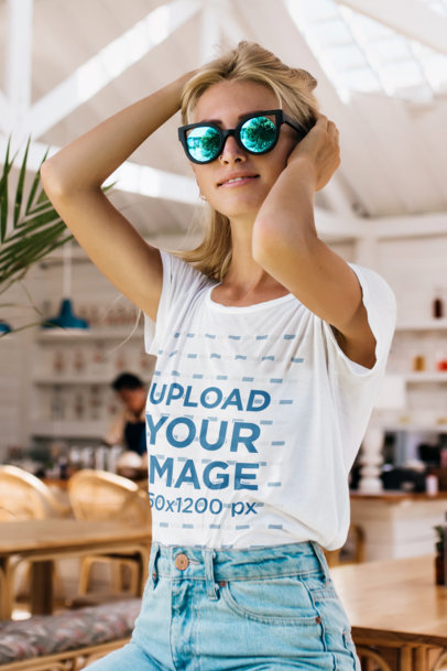 T-Shirt Mockup Featuring a Woman With Cool Sunglasses Posing Near a Coffee Shop