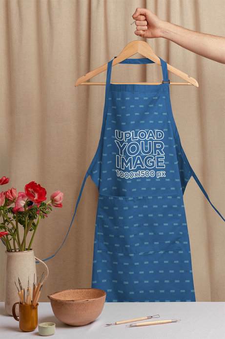 Mockup of an Artist's Apron on a Hanger Behind a Work Table
