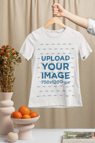 Mockup of a Woman's Hand Holding a Bella Canvas T-Shirt on a Hanger