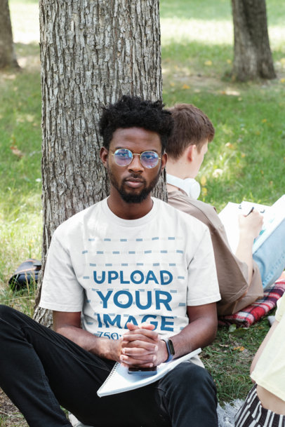 Round-Neck T-Shirt Mockup Featuring a Serious Man Sitting Against a Tree
