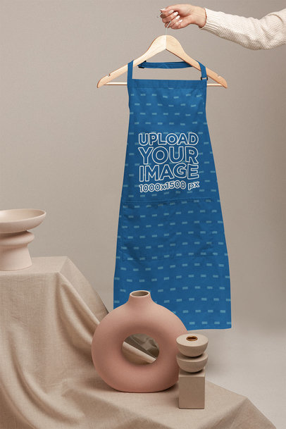 Mockup Featuring a Woman’s Hand Holding a Hanger With an Apron