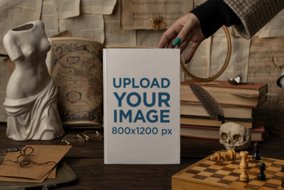 Mockup of a Woman Holding a Hard Cover Book Featuring a Dark Academia Set