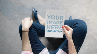 Teenager Girl Holding a Flyer Video Mockup While Sitting In A Concrete Floor
