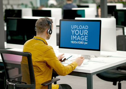 Mockup of a Man Working on an iMac at His Office