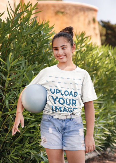 Knotted Tee Mockup of a Happy Girl Holding a Ball by Some Plants