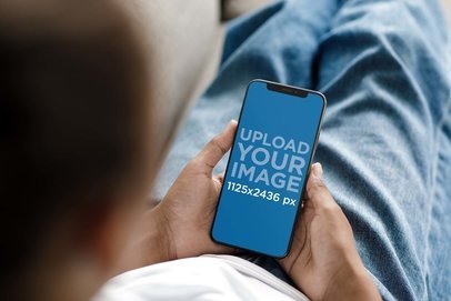 Mockup of a Man Using an iPhone 13 While Lying on a Couch