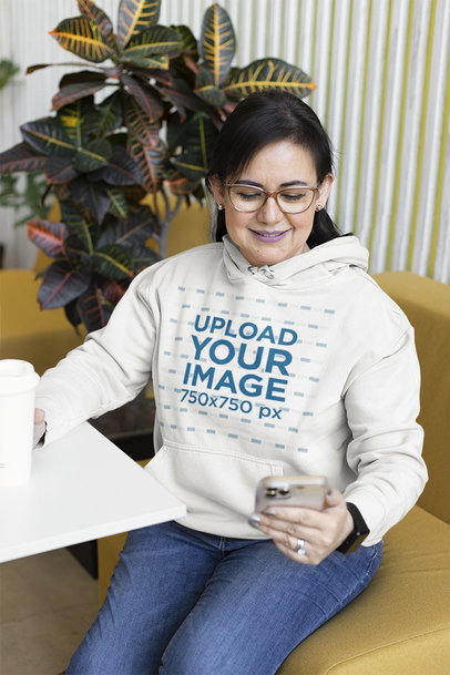 Hoodie Mockup of a Woman Checking Her Smartphone and Drinking Coffee 