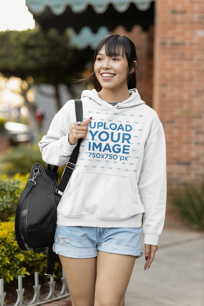 Mockup of a Smiling Woman Wearing a Pullover Hoodie and Carrying a Bag