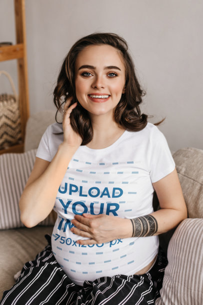 T-Shirt Mockup Featuring a Pregnant Woman With a Tattoo Sitting at Home
