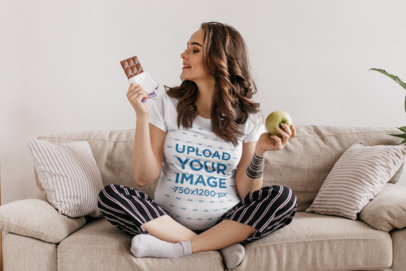 Round-Neck T-Shirt Mockup of a Pregnant Woman Holding Food on a Couch