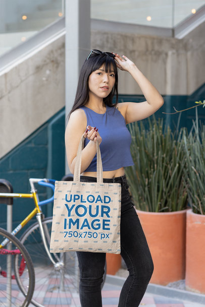 Mockup of a Woman with Sunglasses Holding a Sublimated Tote Bag