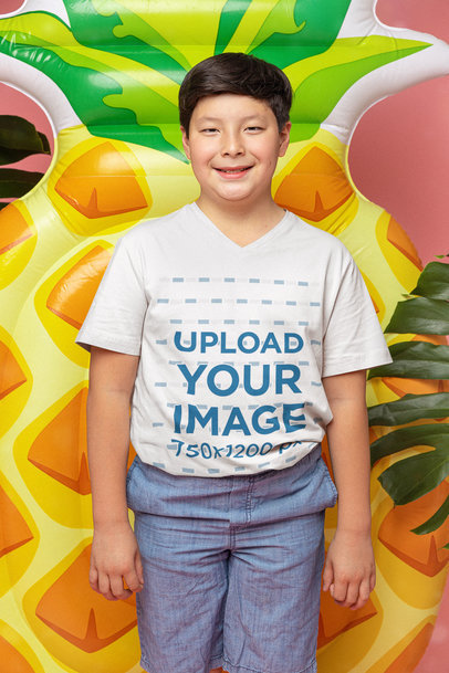 Mockup of a Smiling Kid Wearing a V-Neck Tee with a Pineapple Float Raft in the Background m25626