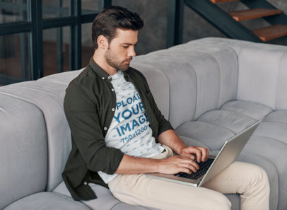 T-Shirt Mockup of a Bearded Man on a Couch Using His Laptop