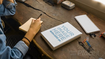 Girl Writing in her Notepad With a Book Video Beside it a13969