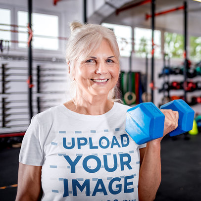 T-Shirt Mockup Featuring a Happy Senior Woman Holding a Dumbbell