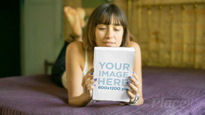 Young Woman Looking at a Book Video While in Her Purple Bed