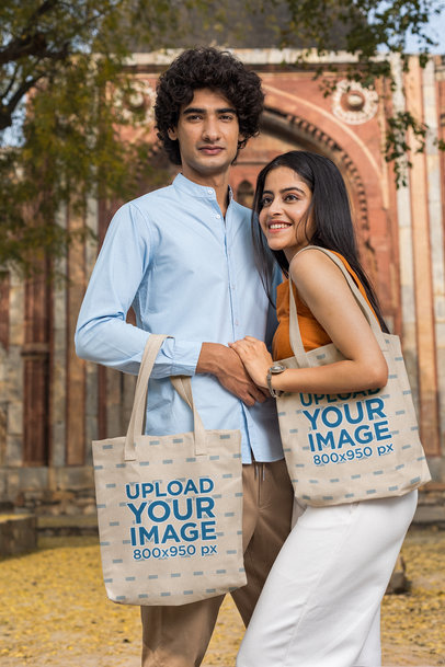 Mockup of a Couple Posing Outside of a Temple While Holding Tote Bags