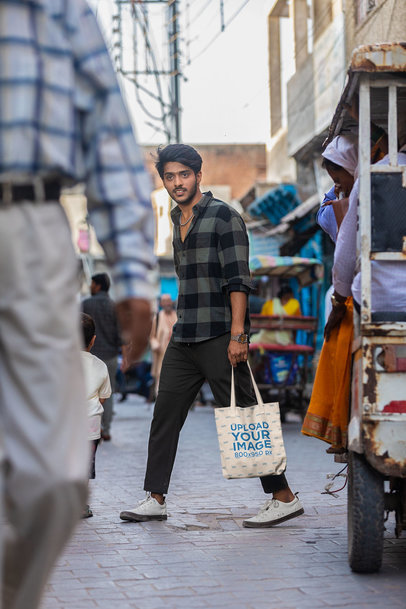 Mockup of a Young Man Walking with a Tote Bag in a Busy Street