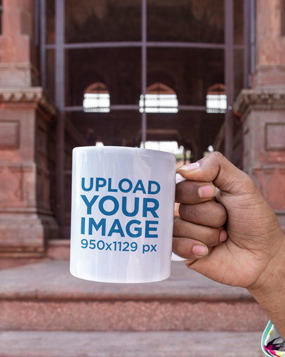 Mockup of a Person Holding an 11 Oz Mug in Front of a Beautiful Building m26125