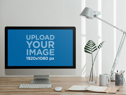 Mockup of an iMac Placed over a Wooden Desk Featuring a Plant and a Notebook