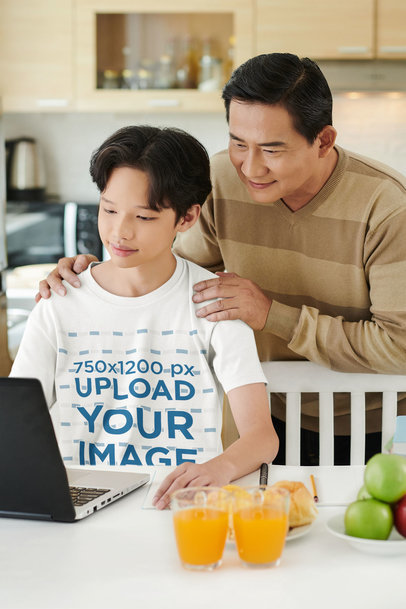 T-Shirt Mockup Featuring a Young Boy Using a Laptop with His Father Standing Behind Him