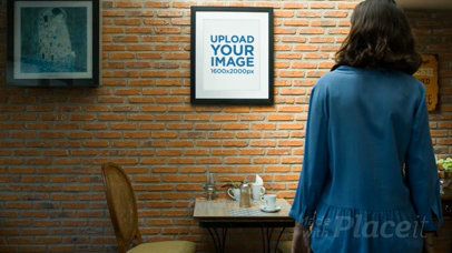 Woman at a Coffee Shop Looks at a Framed Art Print Video on a Bricks Wall