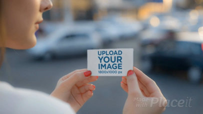 Pretty Woman Holding A Business Card Video Mockup in the City While Cars Passing By