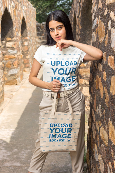 T-Shirt Mockup of a Woman Holding a Tote Bag By a Stone Arch