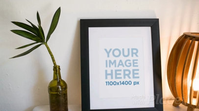 Framed Art Print Video on a Night Table With a Lamp and a Plant Nearby