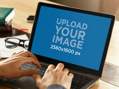 Mockup of a Man Working on His MacBook with His Glasses Over His Desk