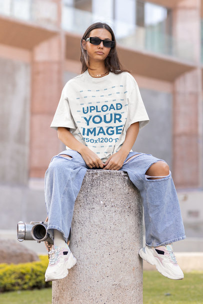Oversized Tee Mockup of a Young Woman Sitting on a Concrete Pillar