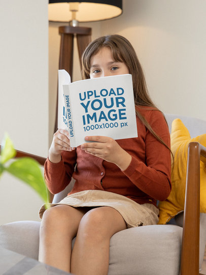 Mockup of a Girl Looking Over a Square Book at Home