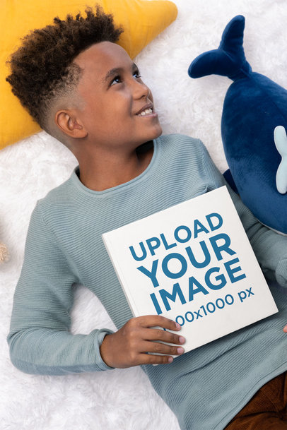 Mockup Featuring a Boy Holding a Book on His Bed