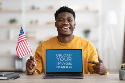 Mockup of a Happy Man Holding a Small American Flag and Pointing at a Macbook Pro