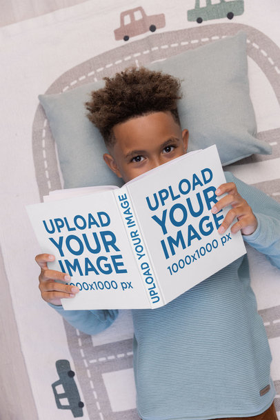 Mockup of a Boy Lying on His Bed and Holding a Hard-Cover Book