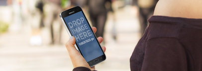 Mockup Featuring a Woman Holding a Samsung Galaxy in Portrait Position on a Busy Street