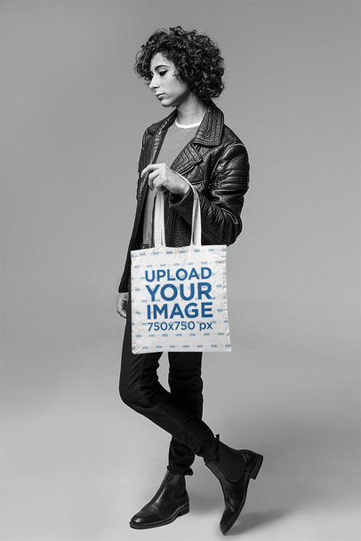 Black-and-White Mockup of a Serious-Looking Man Holding a Tote Bag at a Studio