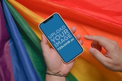 Mockup of a Person Holding an iPhone 12 with a Gay Pride Flag in the Background