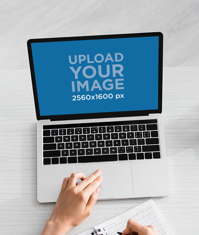 Mockup of a Woman Working on a Macbook and Writing on a Notebook