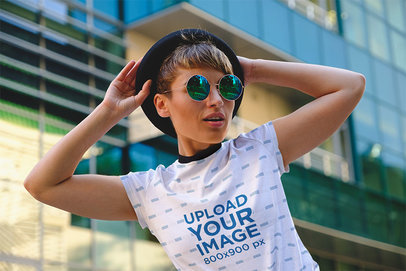 T-Shirt Mockup Featuring a Cool Woman Posing by a Glass Building