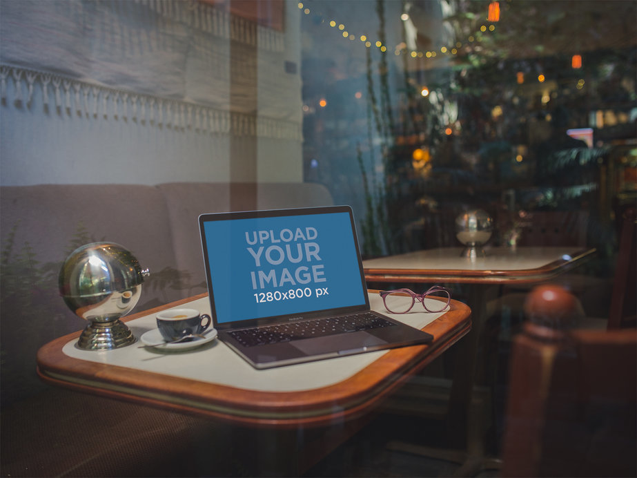 Mockup of a MacBook Through the Window on a Restaurant Table with a Christmas Tree Behind It