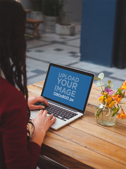 Mockup of a Woman Using a MacBook Pro on a Wooden Table with some Flowers
