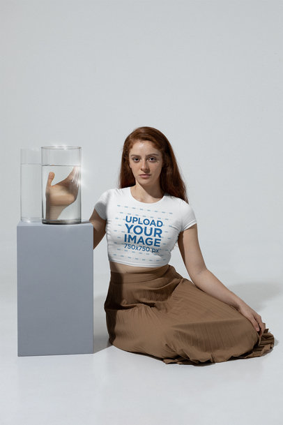 Mockup of a Red-Haired Woman With a Crop Top Tee Sitting Next to a Glass Vase m28398