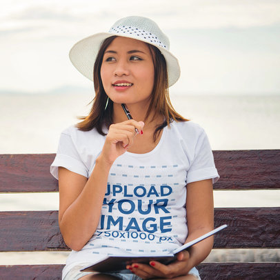 T-Shirt Mockup of a Woman Sitting on a Bench with a Notebook and a Pen m17940 r-el2