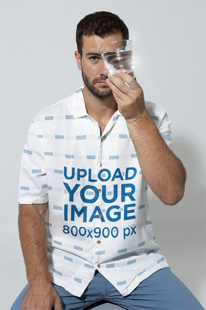 Button-Up Shirt Mockup of a Man Holding a Glass of Water Close to His Eye