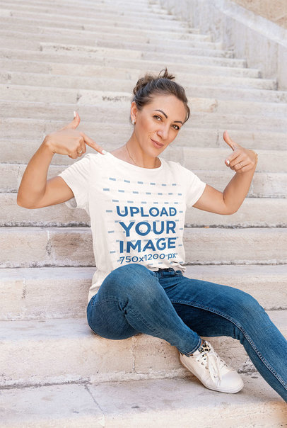 Mockup of a Woman Pointing at her T-Shirt While Posing by the Stairs