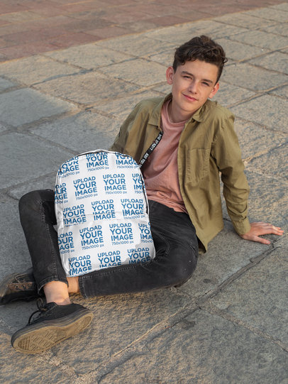 Backpack Mockup Featuring a Happy Teenage Boy Sitting on the Floor