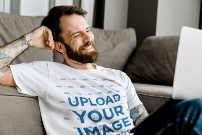 T-Shirt Mockup Featuring a Smiling Bearded Man Leaning on a Couch