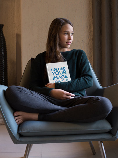 Little Girl Holding a Book Mockup Sitting on an Armchair a19077