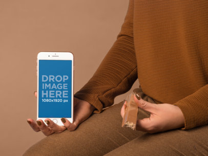 Woman Dressing in Brown Holding an iPhone 8 Mockup and a Chocolate Against a Brown Background a19245